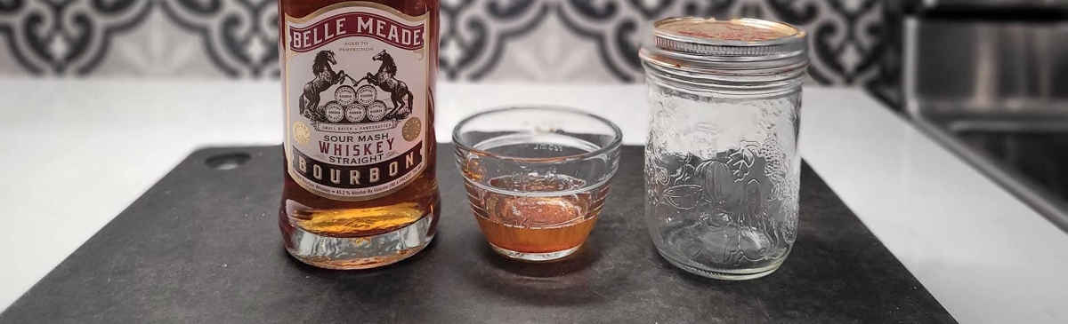 A bottle of bourbon and a small bowl of bacon fat on a counter.