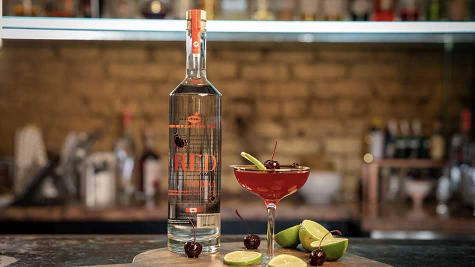 A cocktail and bottle of vodka on a bar.