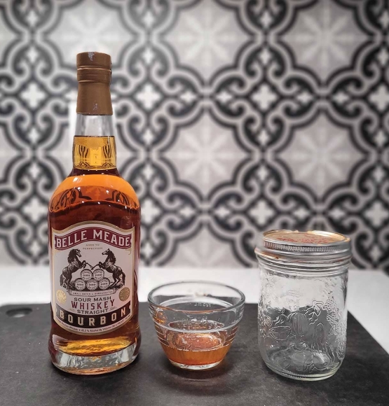 A bottle of bourbon and a small bowl of bacon fat on a counter.