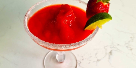 Frozen Strawberry Margarita with a strawberry and lime on the rim.