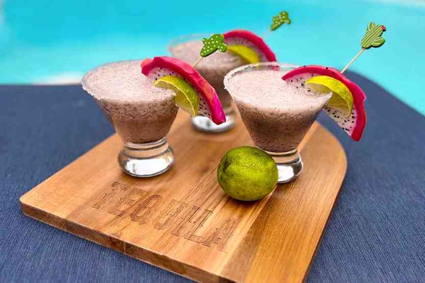 3 Dragon Fruit Margaritas on a tequila cutting board by a pool.